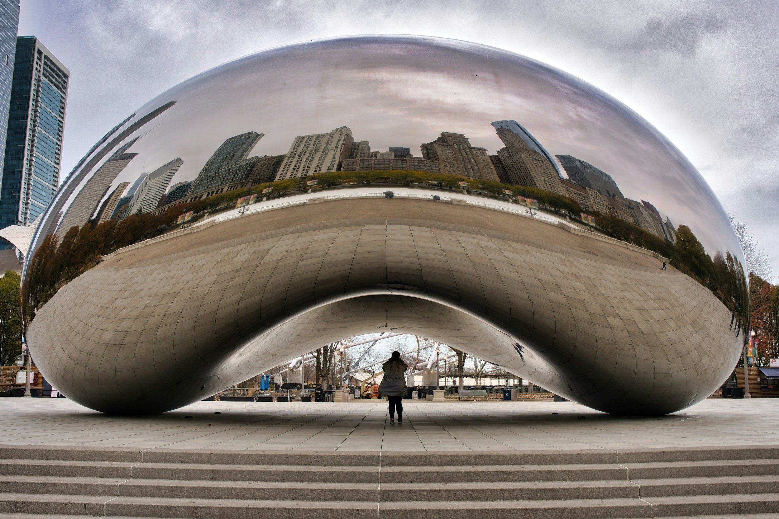 The Cloud Gate sculpture, also known as 'The Bean,' located in Millennium Park Chicago, is a shiny, metallic, bean-shaped art installation reflecting the city skyline, trees, and visitors.