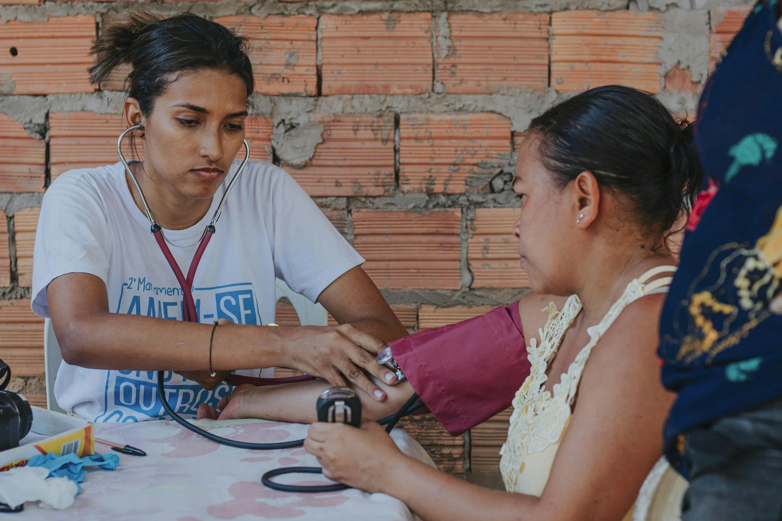 A healthcare worker measuring a woman's blood pressure with a blood pressure cuff during a medical outreach event.