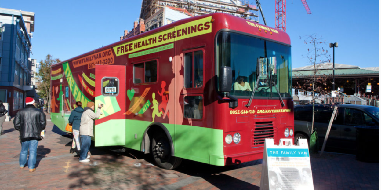 A red and green mobile health screening unit called "The Family Van" offering free health screenings, with people standing in line outside the van on a city street.