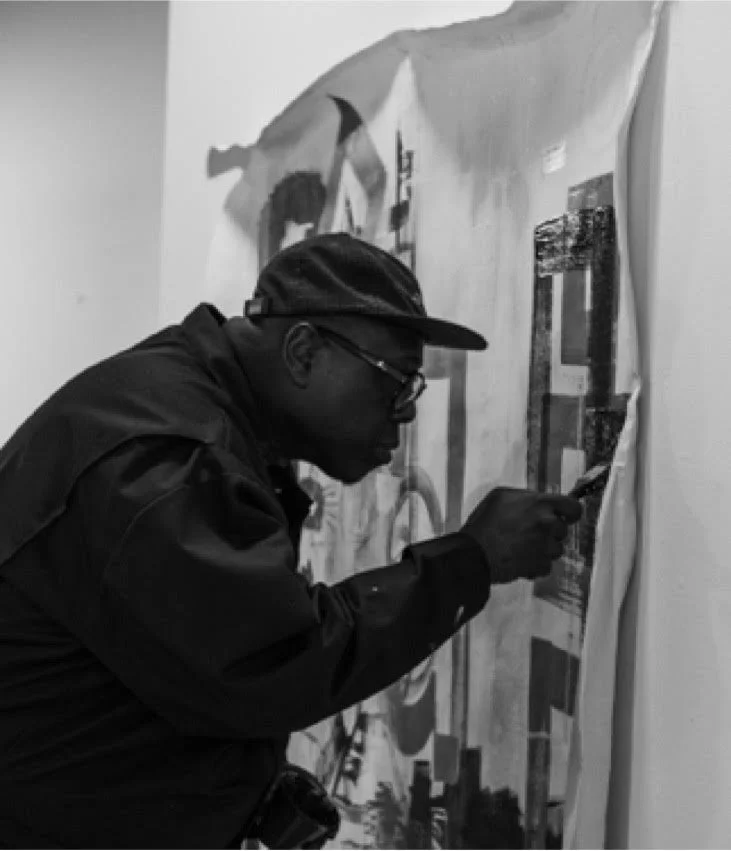 A man wearing a cap and dark jacket is taking a photo of a large mural on a wall.