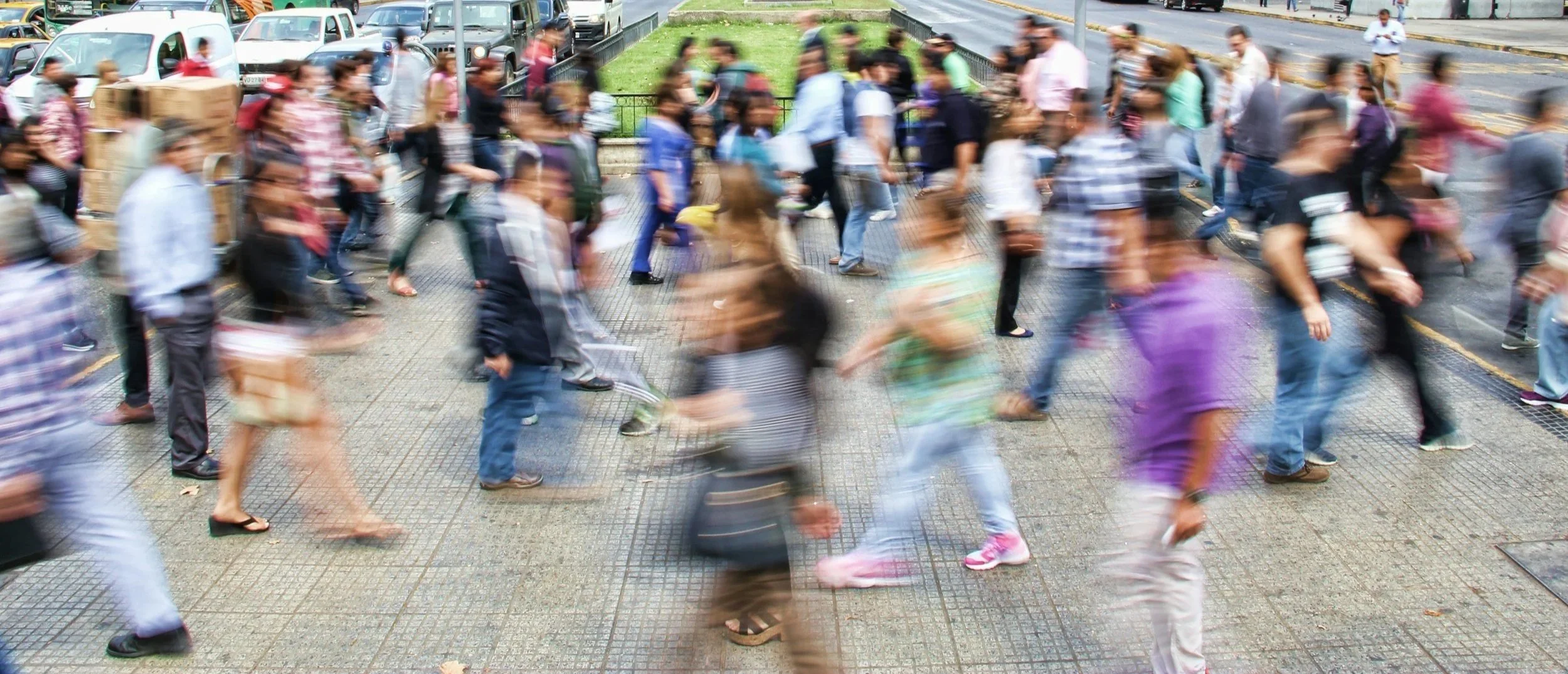 A crowded crosswalk with many pedestrians walking in various directions on a city sidewalk.