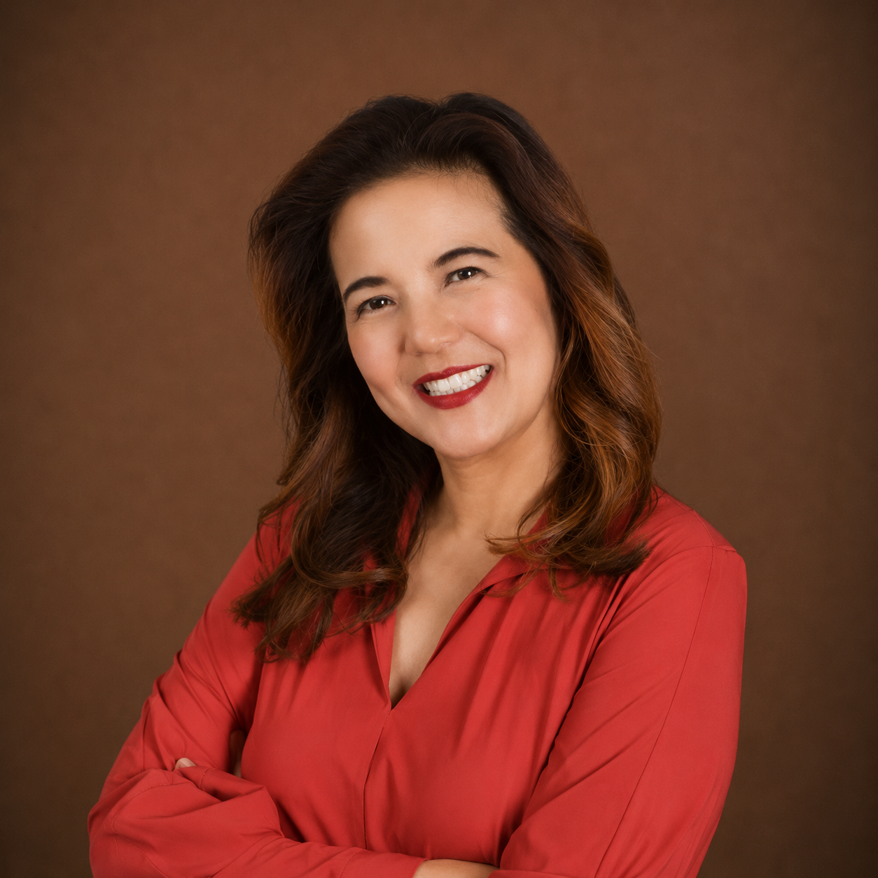 A woman with wavy brown hair smiling, wearing a red blouse, against a brown background.