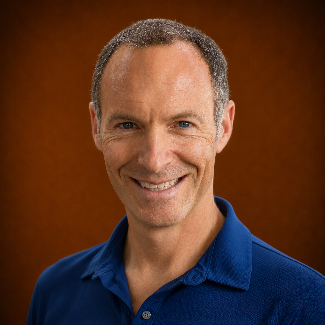 Headshot of a smiling middle-aged man with short, graying hair wearing a blue collared shirt.