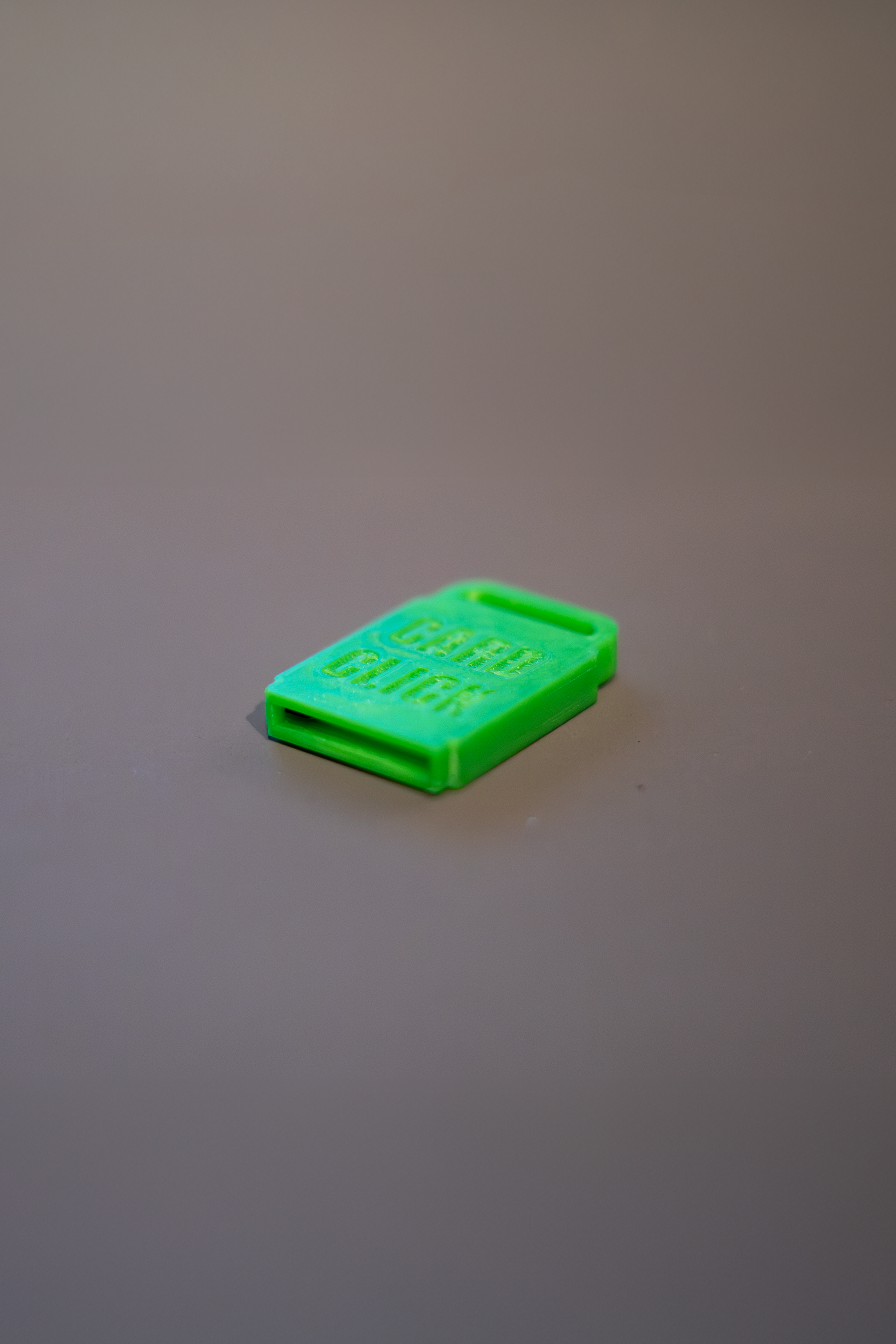 A small green plastic SD card holder with the words 'CARD CLICK' embossed on it, positioned on a gray surface.