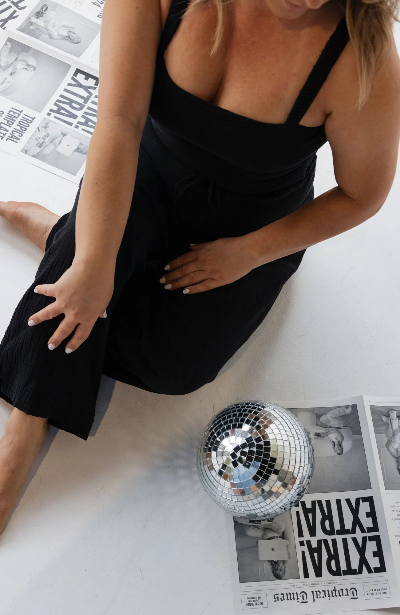 A close up detail shot of Alaina wearing a black linen set surrounded by newspapers