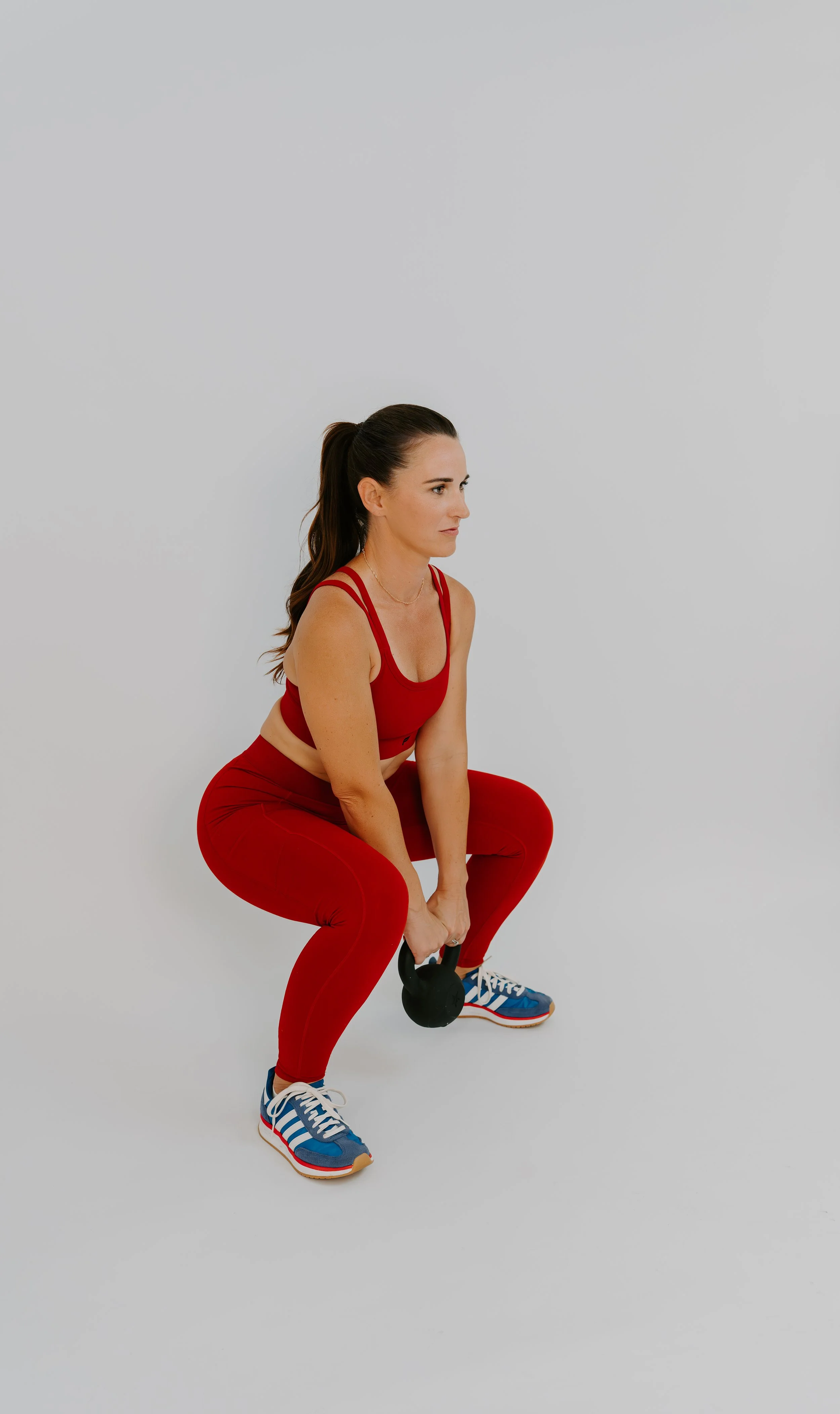 A fitness coach wearing a matching red activewear set and lifting a kettlebell in a white studio setting