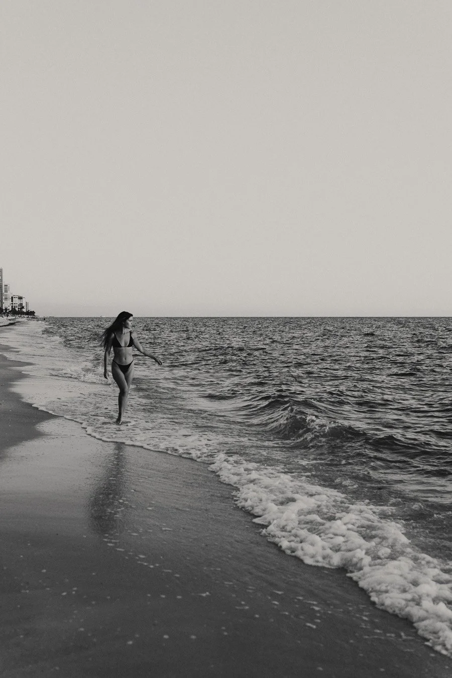 Black and white beach portrait of woman standing along the shoreline in Naples, Florida during lifestyle branding session