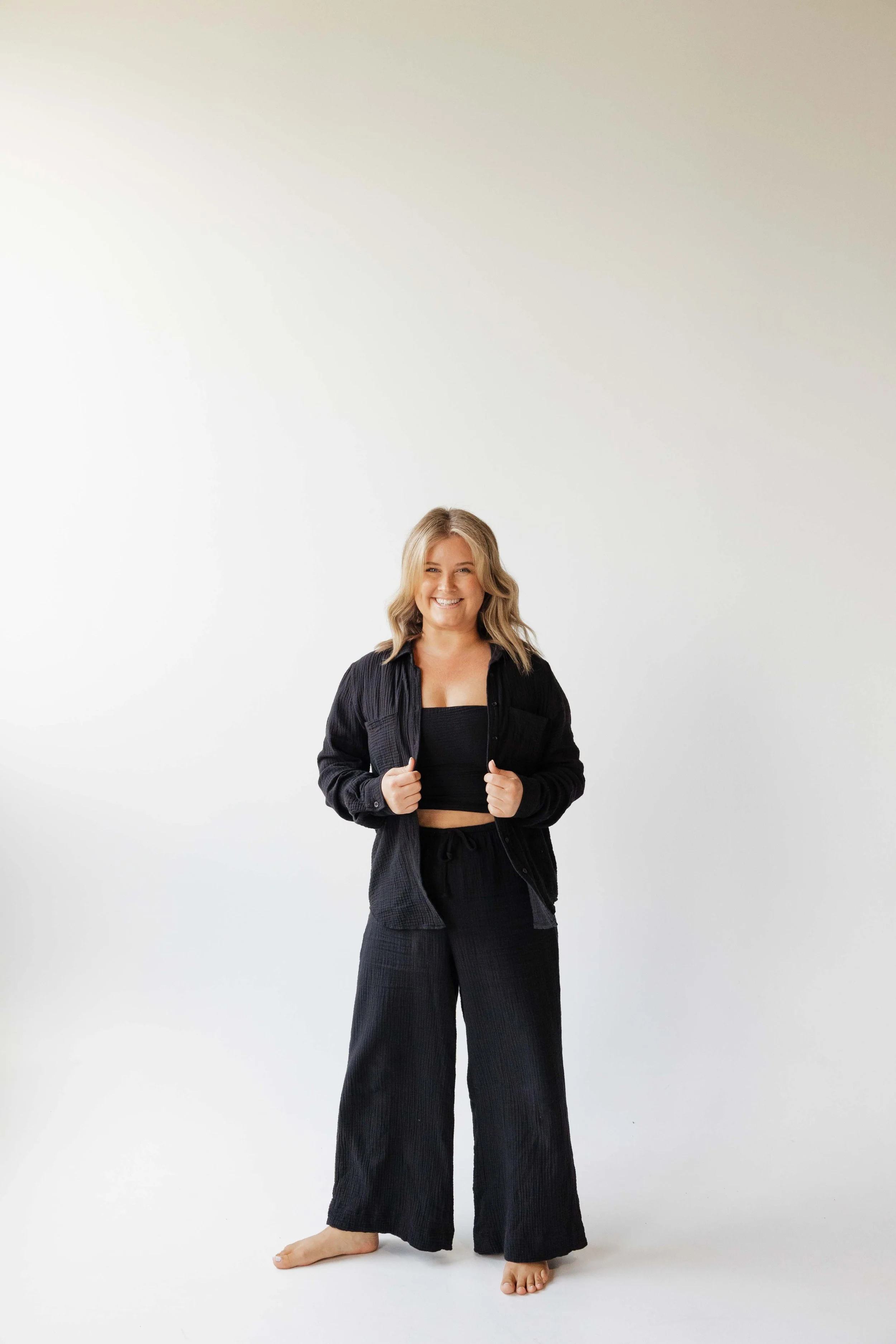 Alaina, owner and photographer, stands proudly holding the edges of her black linen shirt and smiling at the camera during her studio photoshoot in St. Pete
