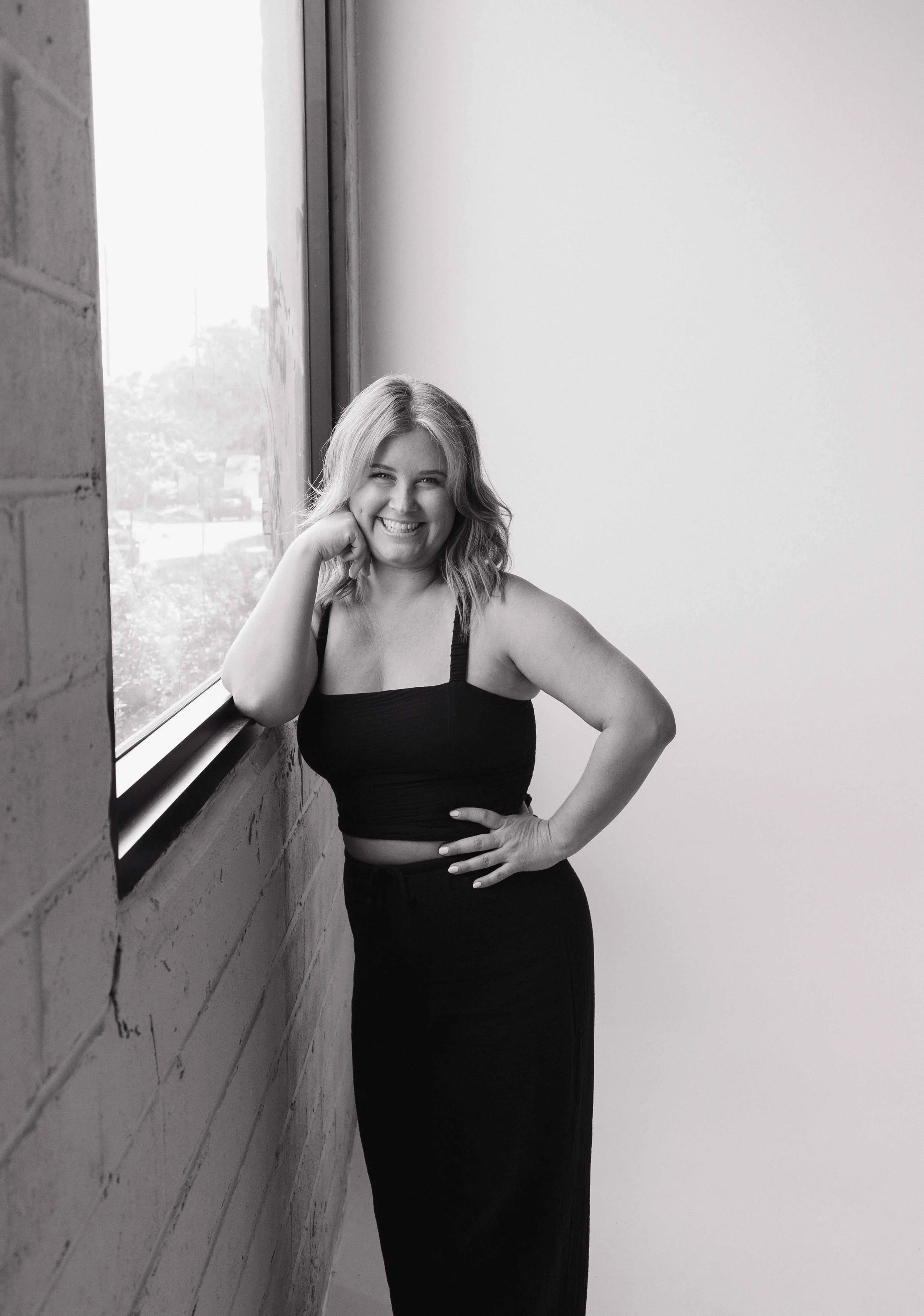 Alaina smiles at the camera while leaning against a window in a studio in St. Pete, Florida