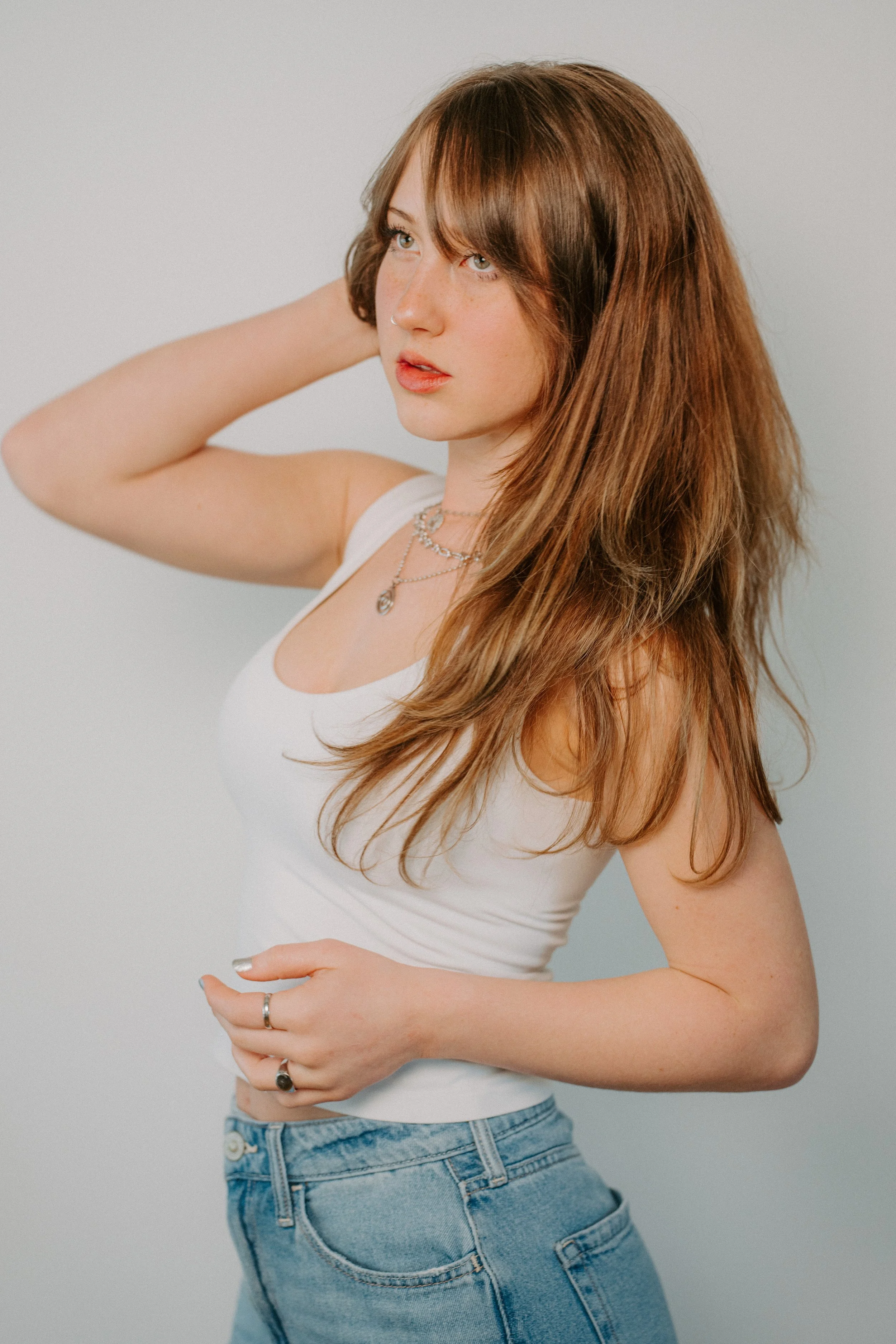 young woman wearing white tank top and jeans looks off to the left during a modern studio brand photography session in Fort Myers