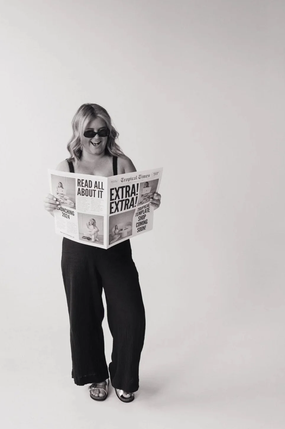 A black and white image of Alaina reading a newspaper while smiling and laughing