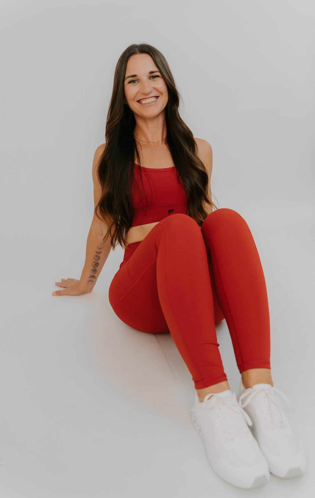 woman wearing matching red activewear set leans back and smiles at the camera during a studio photoshoot with Alaina Marie Brand Photography