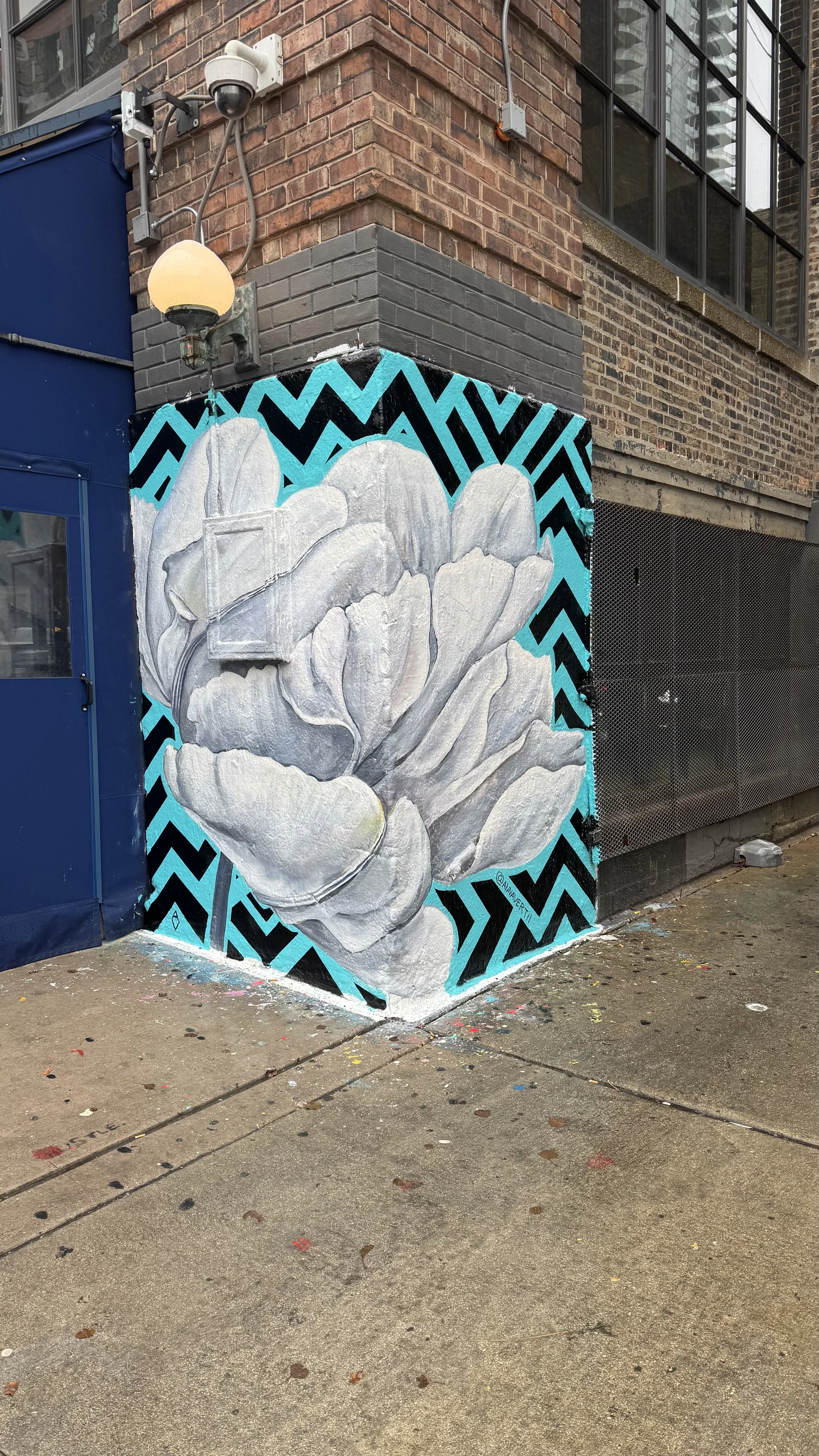 Mural by AnnaV at Soho House Chicago — a large white peony bloom painted on a teal and black chevron background, wrapping around an exterior corner