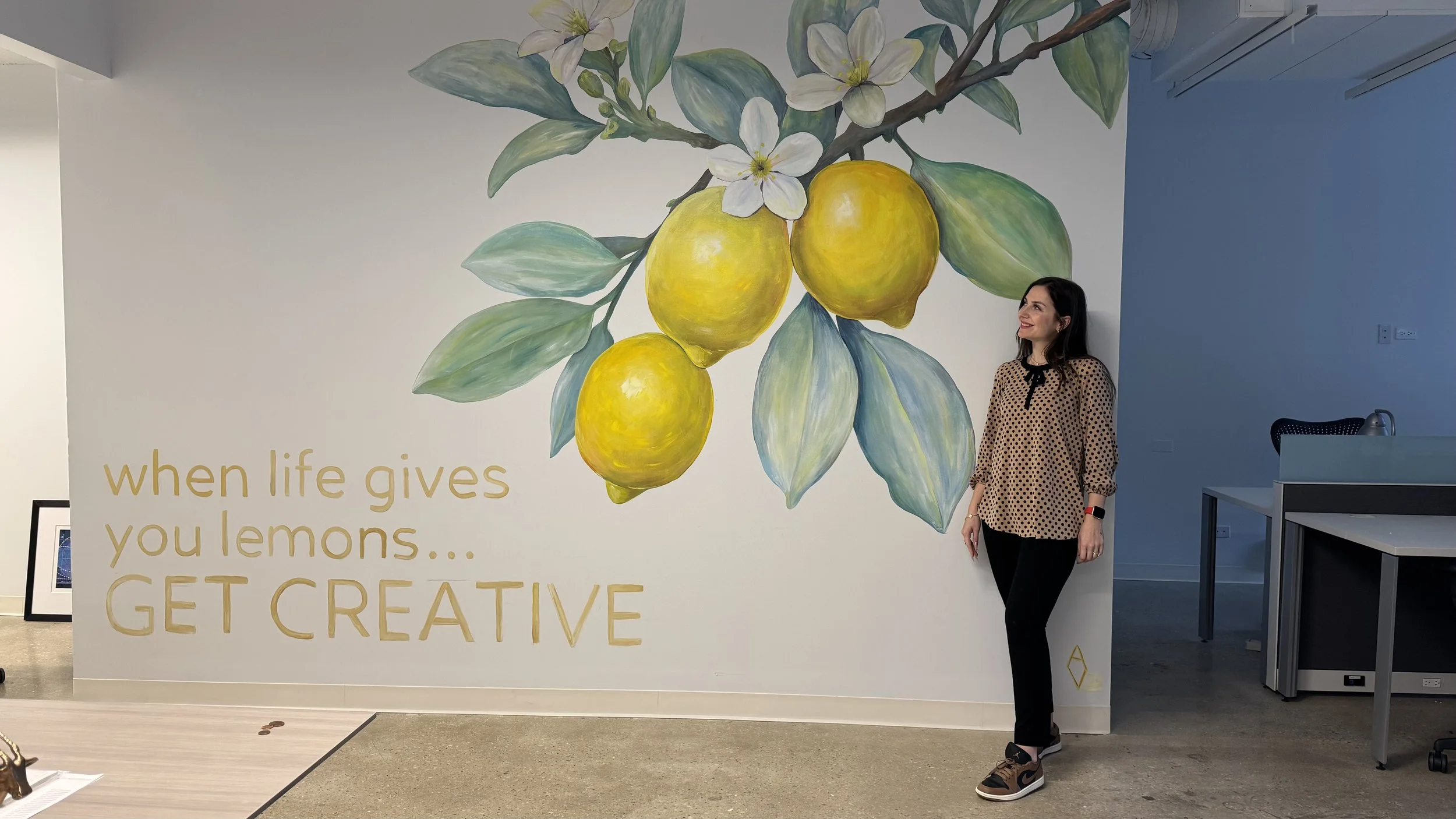 Indoor mural by AnnaV in a Chicago office — a painterly lemon branch with white blossoms above the quote 'When life gives you lemons... Get Creative