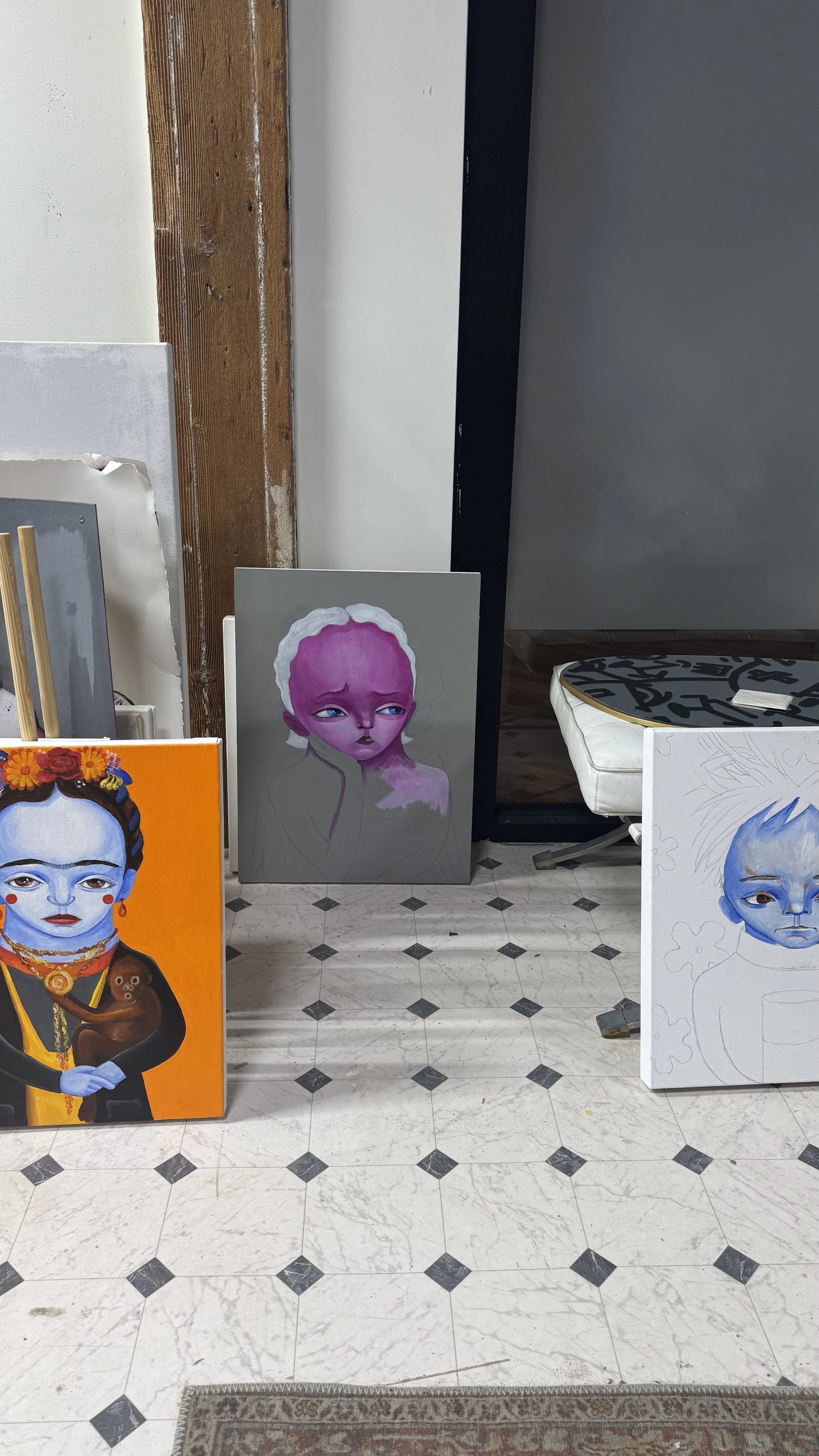 AnnaV's Chicago studio — character paintings in various stages, including a finished Frida portrait, a pink-skinned figure in progress, and a sketched blue character