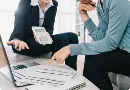 two people at a desk calculating costs on a calculator and computer