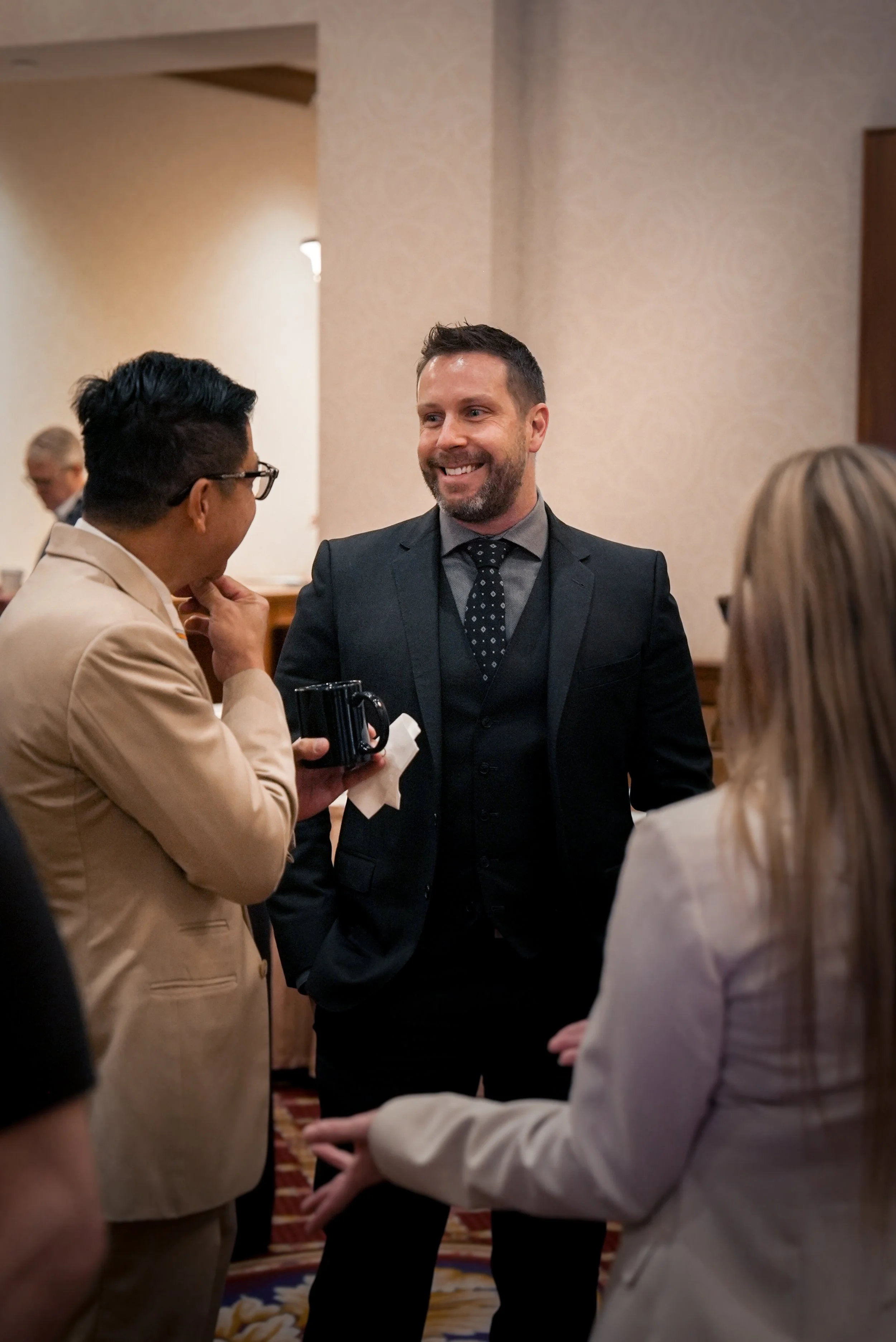 Group of people engaged in conversation at a formal event or gathering in a well-lit room.