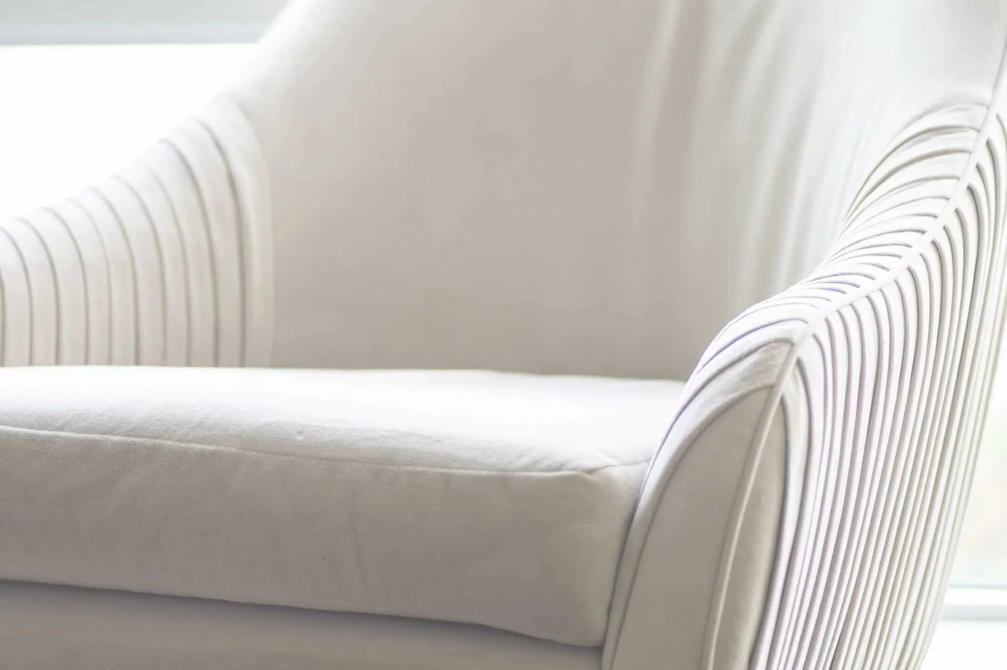 Close-up of a white armchair with ribbed upholstery on the armrests and a cushioned seat.