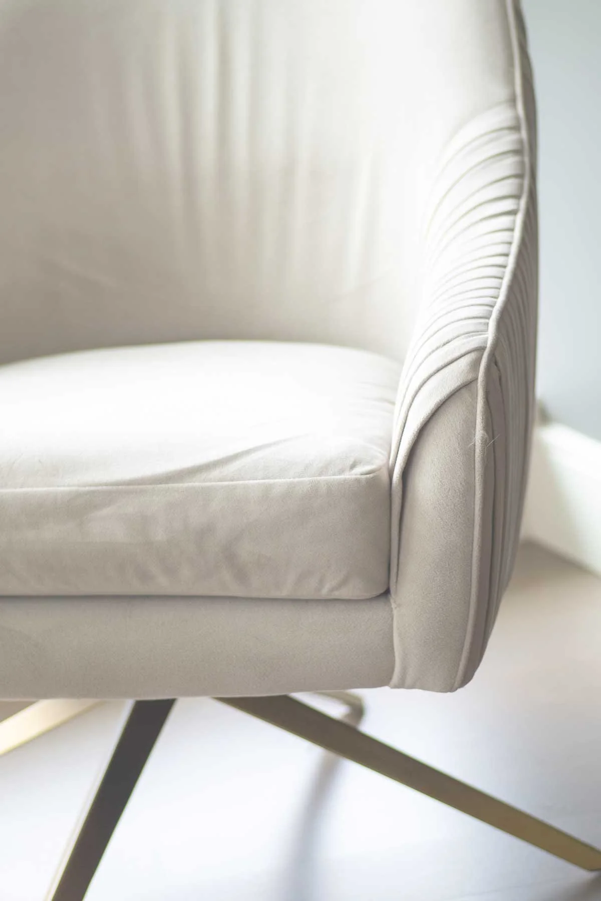 Close-up of a white upholstered armchair with a rounded back and vertical stitching details, supported by black and gold angled legs.