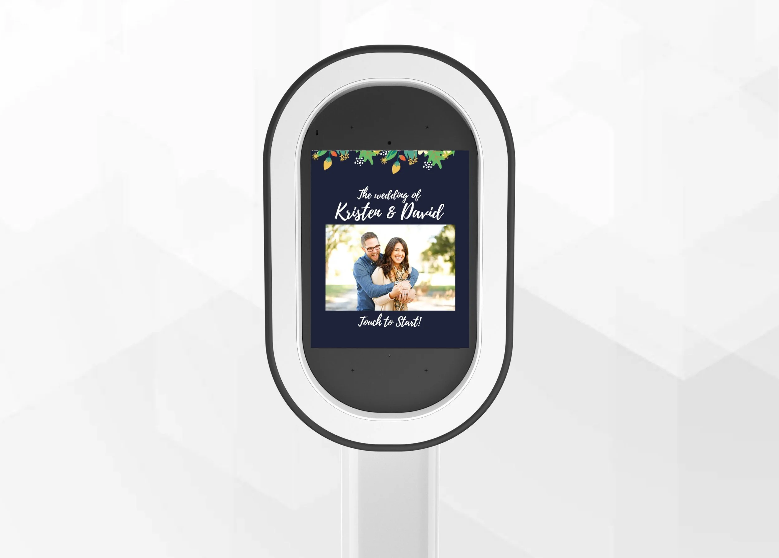 A touchscreen device displays a wedding invitation for Kristen and David, featuring a photo of a smiling couple and decorative greenery at the top, with the text 'The wedding of Kristen & David' and 'Touch to Start!' at the bottom.