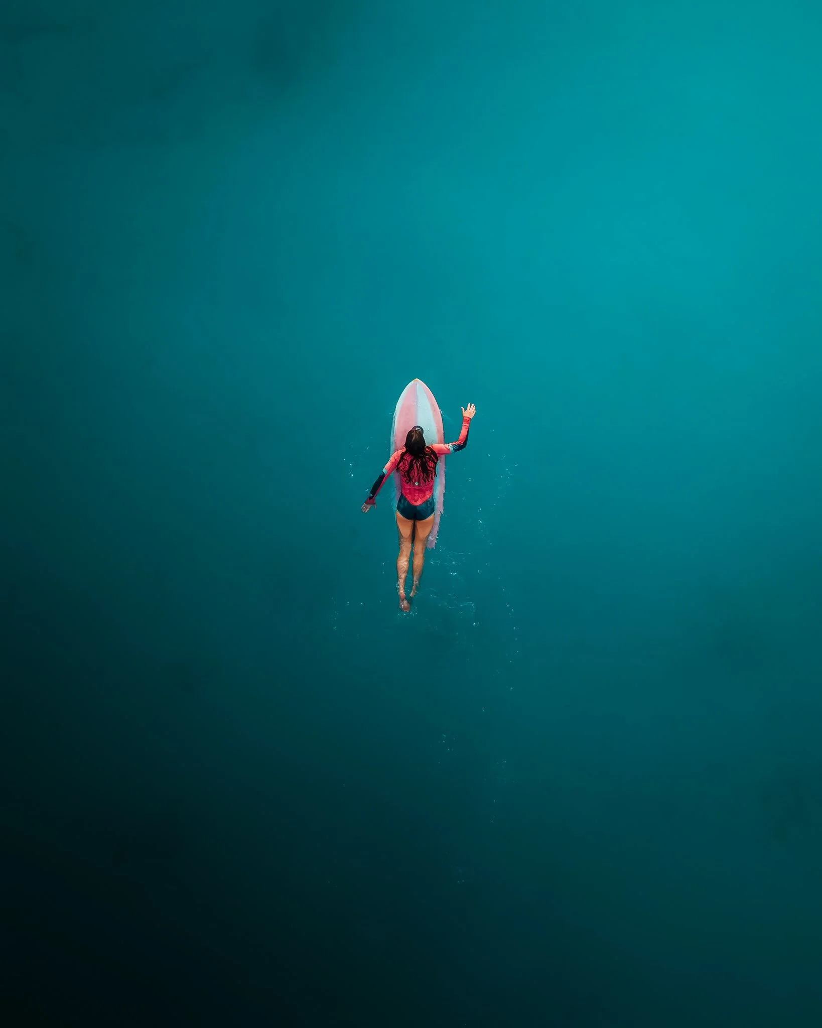 A person with long hair paddleboarding on calm, deep blue water.