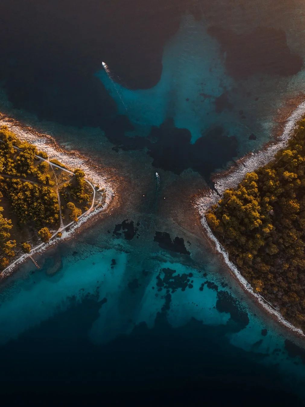 Aerial view of a body of water with a boat and surrounded by trees and a pathway.