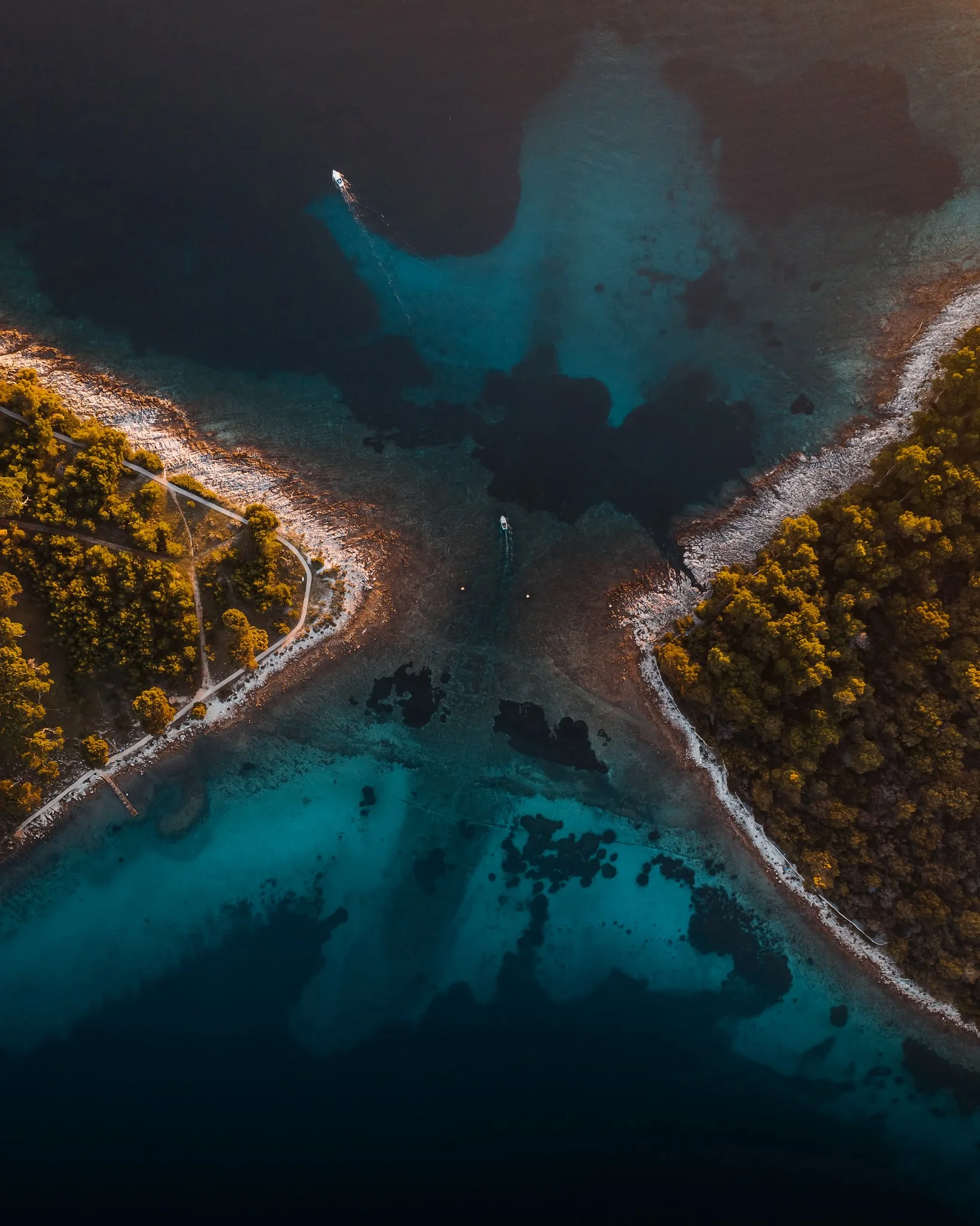 Aerial view of a boat navigating through a scenic cove with clear blue water, surrounded by rocky shoreline and green trees.