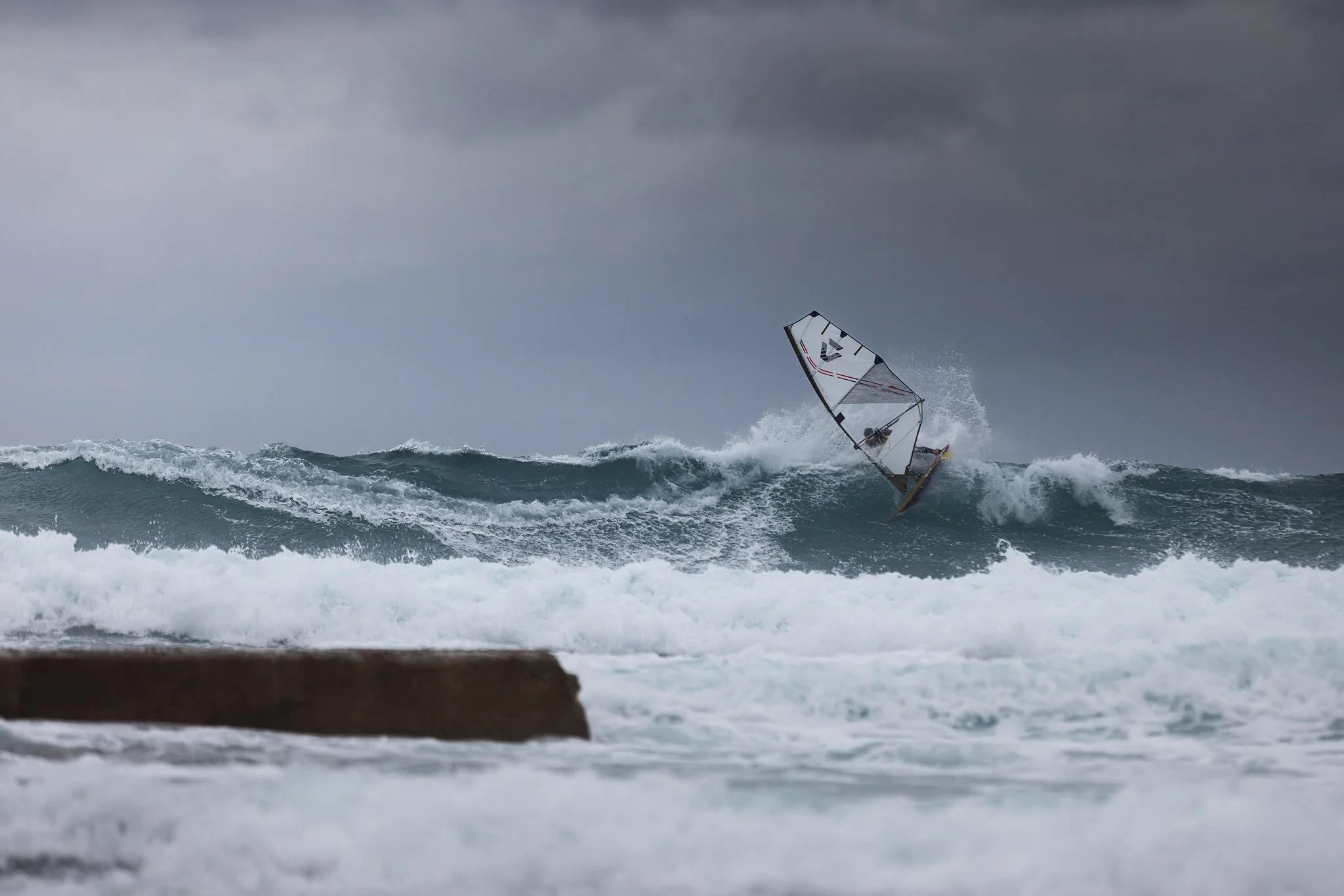 A windsurfer riding a wave during a stormy day with dark clouds in the sky.