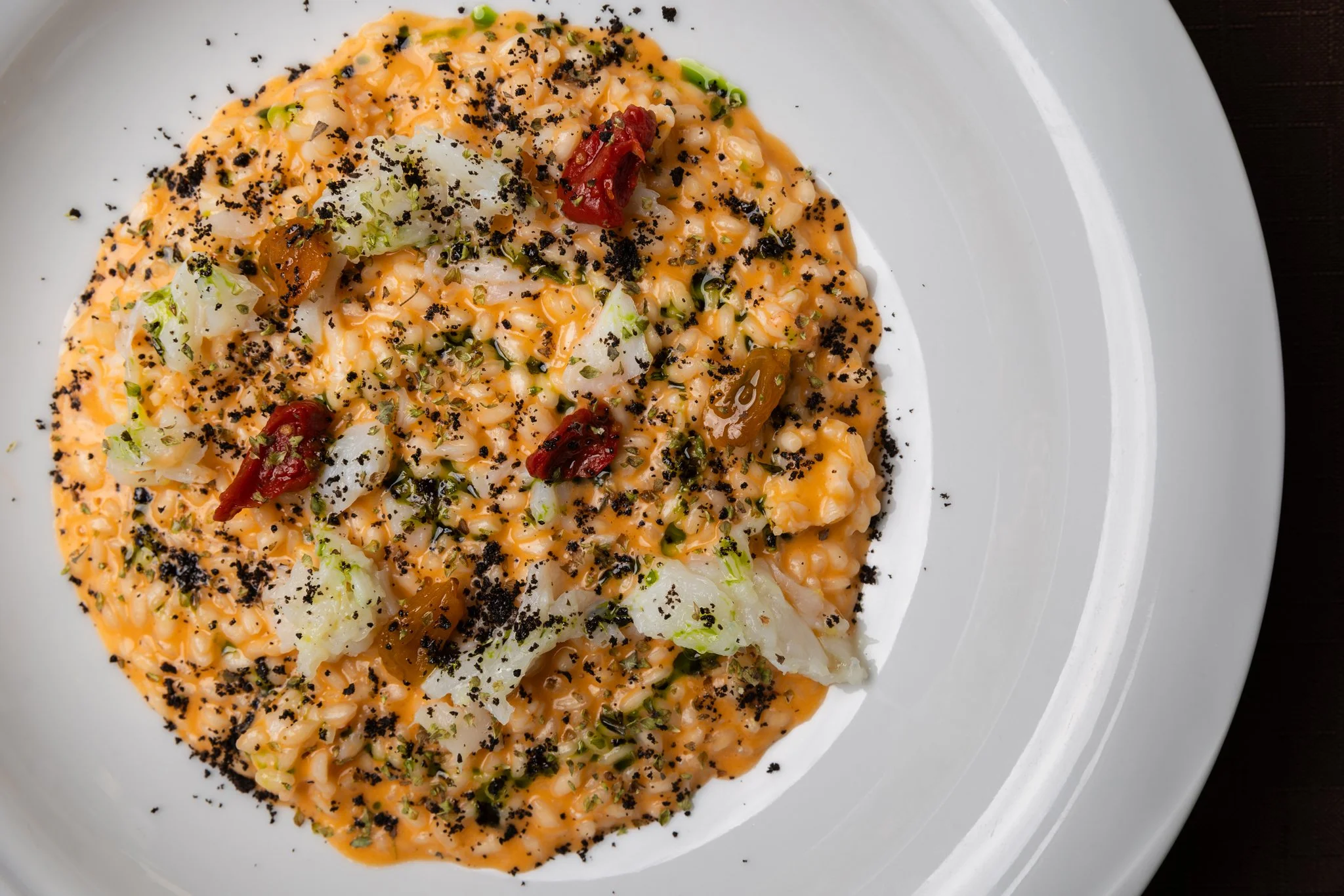 A plate of baked mac and cheese topped with black pepper, chopped green onions, diced tomatoes, and herbs.