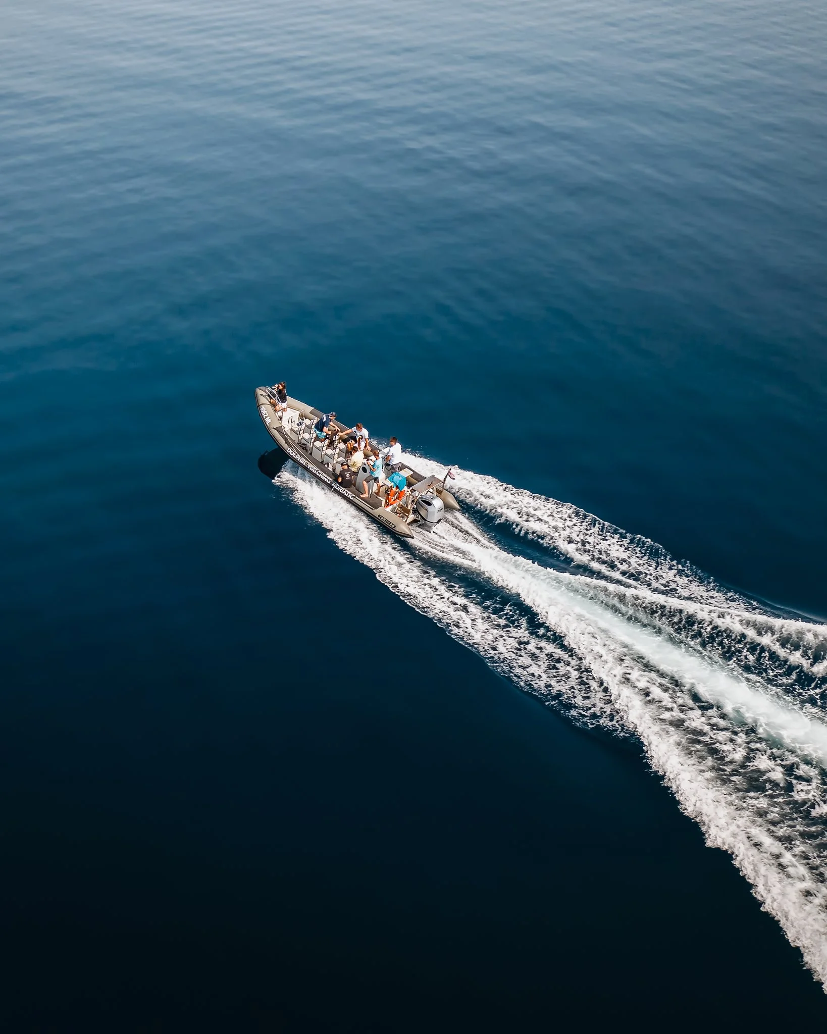 A group of people riding in a motorboat on a large body of water, creating a wake behind it.