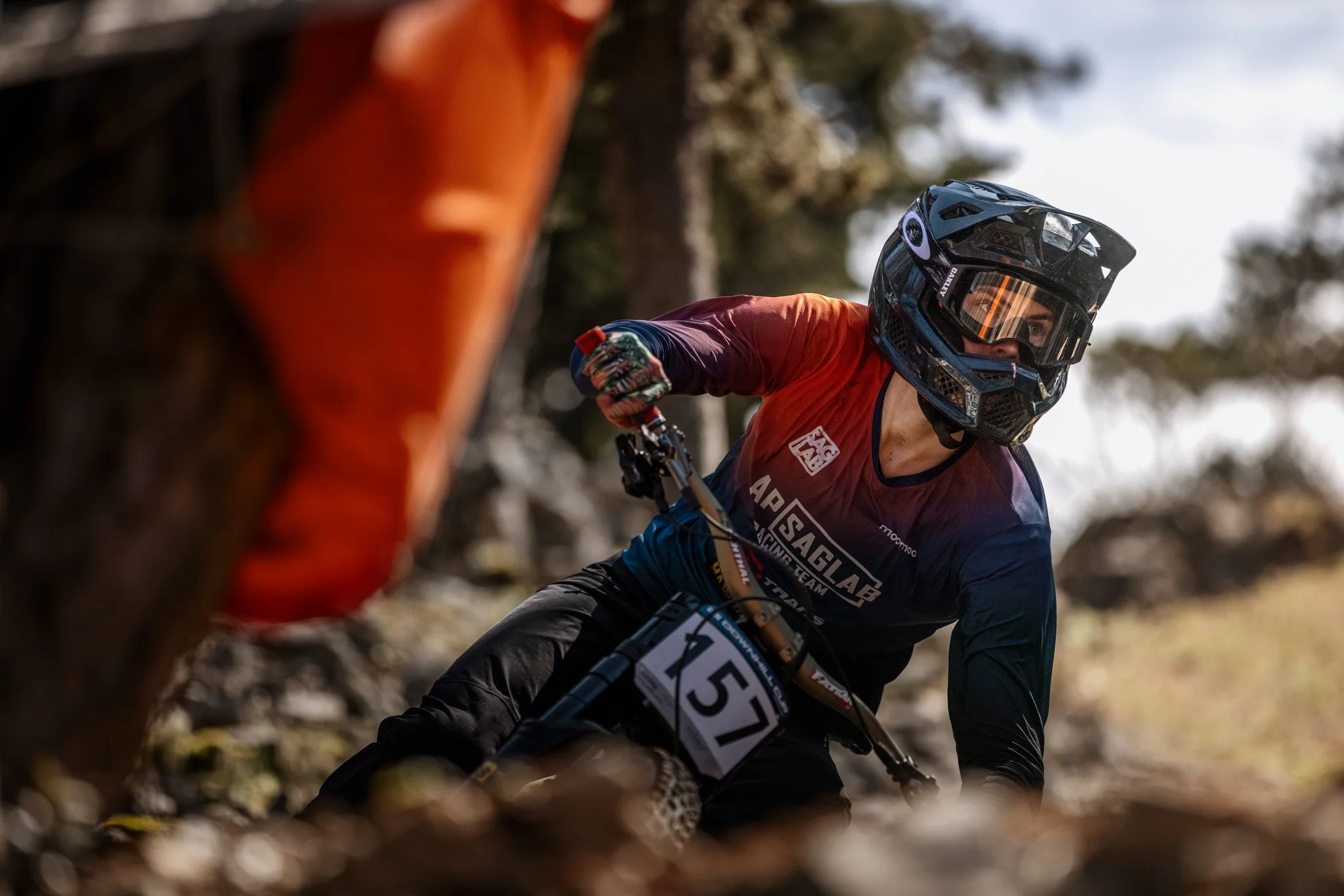 A mountain biker wearing a black helmet and riding gear navigates a trail through a wooded area.