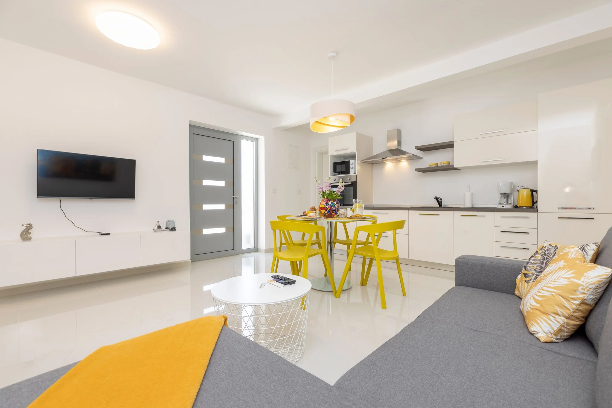 Modern open-concept living room and kitchen with yellow chairs, white cabinets, and a gray sofa with yellow and patterned pillows.