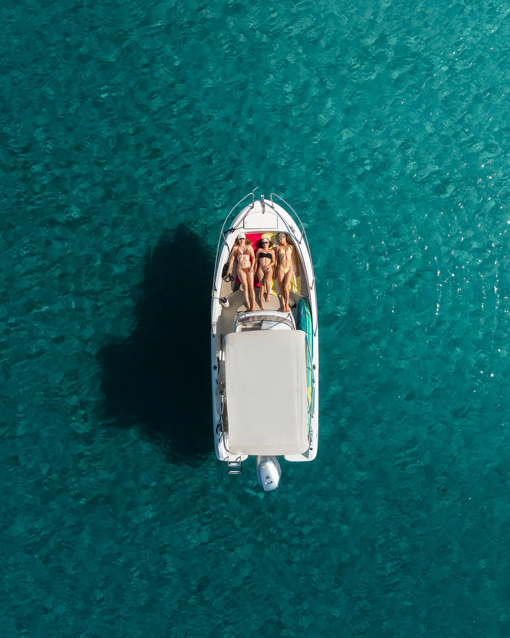 Aerial view of three women sunbathing on a white boat in turquoise water.