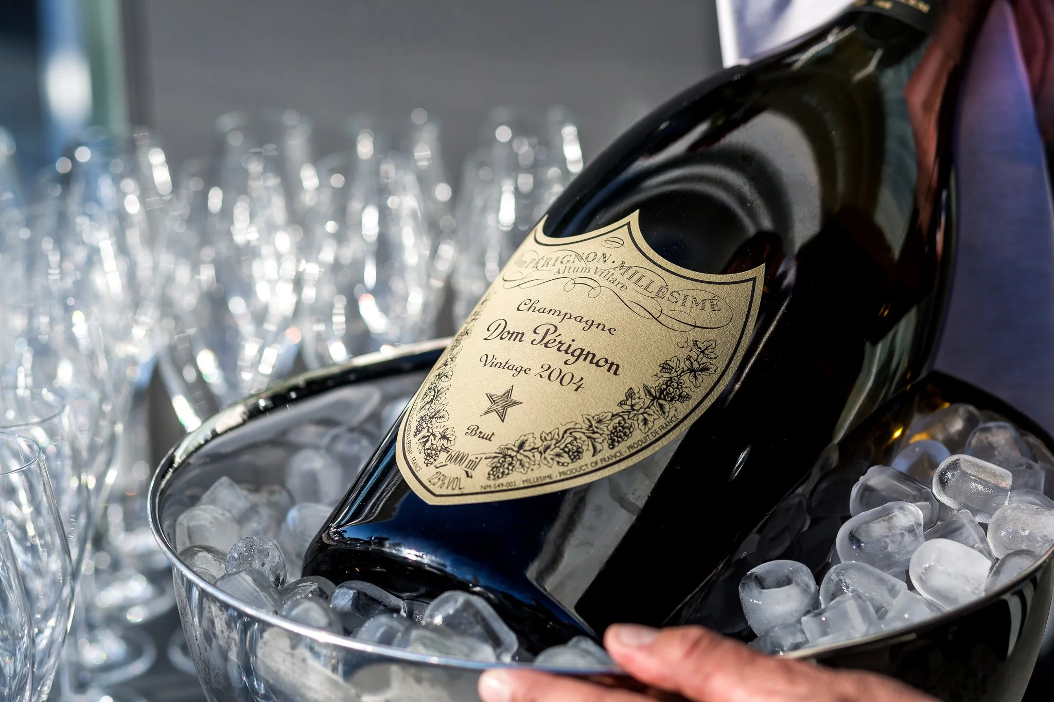 A bottle of Dom Pérignon vintage champagne lying in a silver ice bucket filled with ice, with glasses of sparkling water and ice surrounding it.