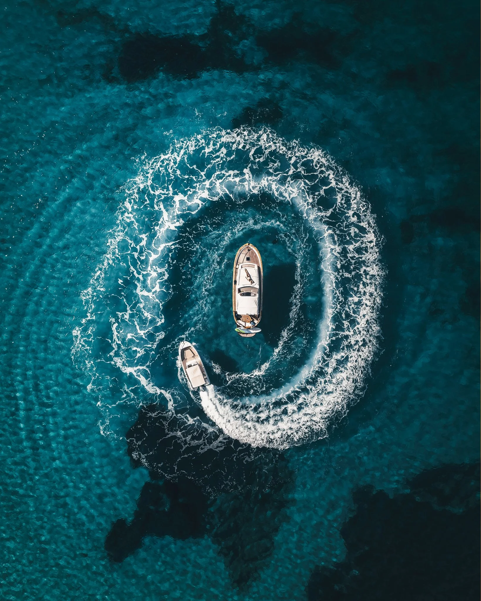 Overhead view of a boat cruising on blue ocean water, leaving white foamy wake behind it.
