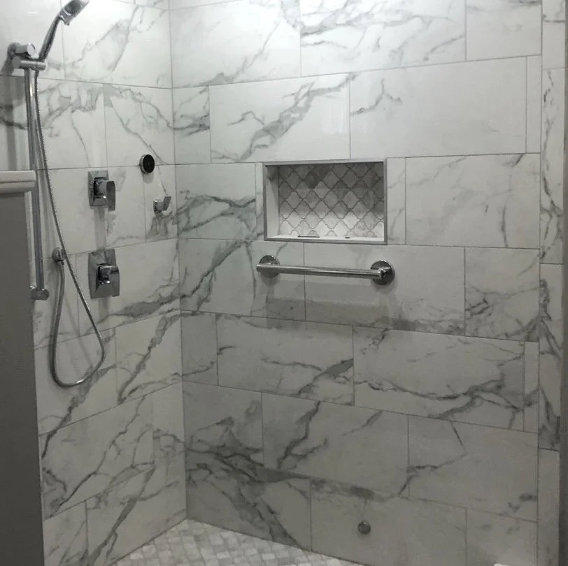 Close-up of a tiled shower niche, horizontal grab bar, handheld shower, and a marble-look porcelain tile in Upper Moreland, PA.
