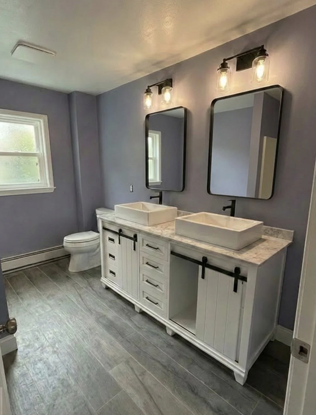 Bathroom remodel with white double Vessel sink vanity, black barn door hardware, marble countertop, and gray wood flooring