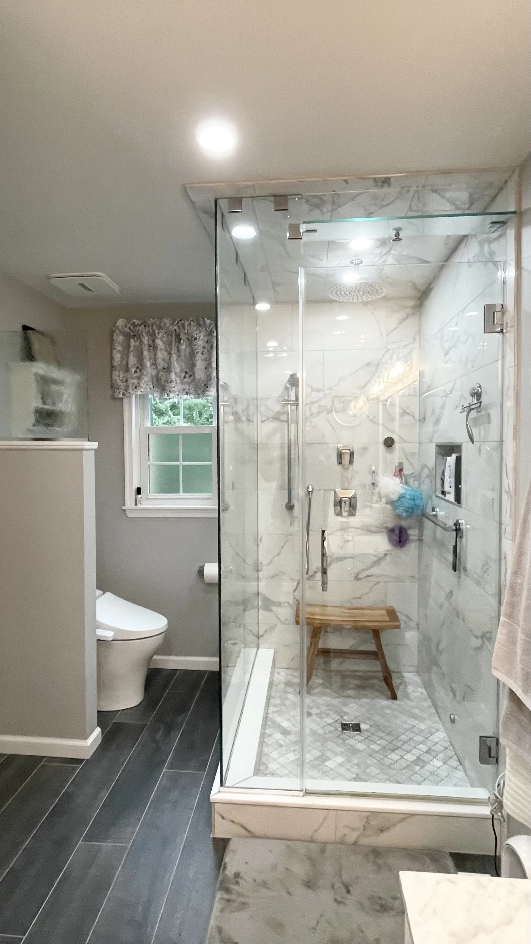 JWD Contractors bathroom remodel in Upper Moreland Township with a frameless glass walk-in shower, marble look tile, mosaic, shower floor, grab bars, and a recessed niche.