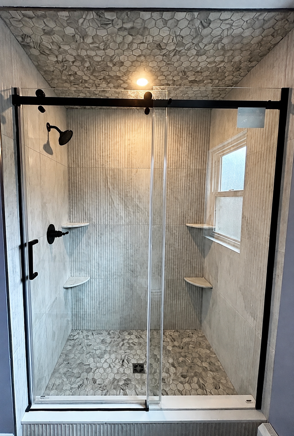 Custom walk-in shower in a Hatboro, PA bathroom remodel with fluted wall tile, mosaic floor and ceiling tile, black hardware, and built-in corner shelving.