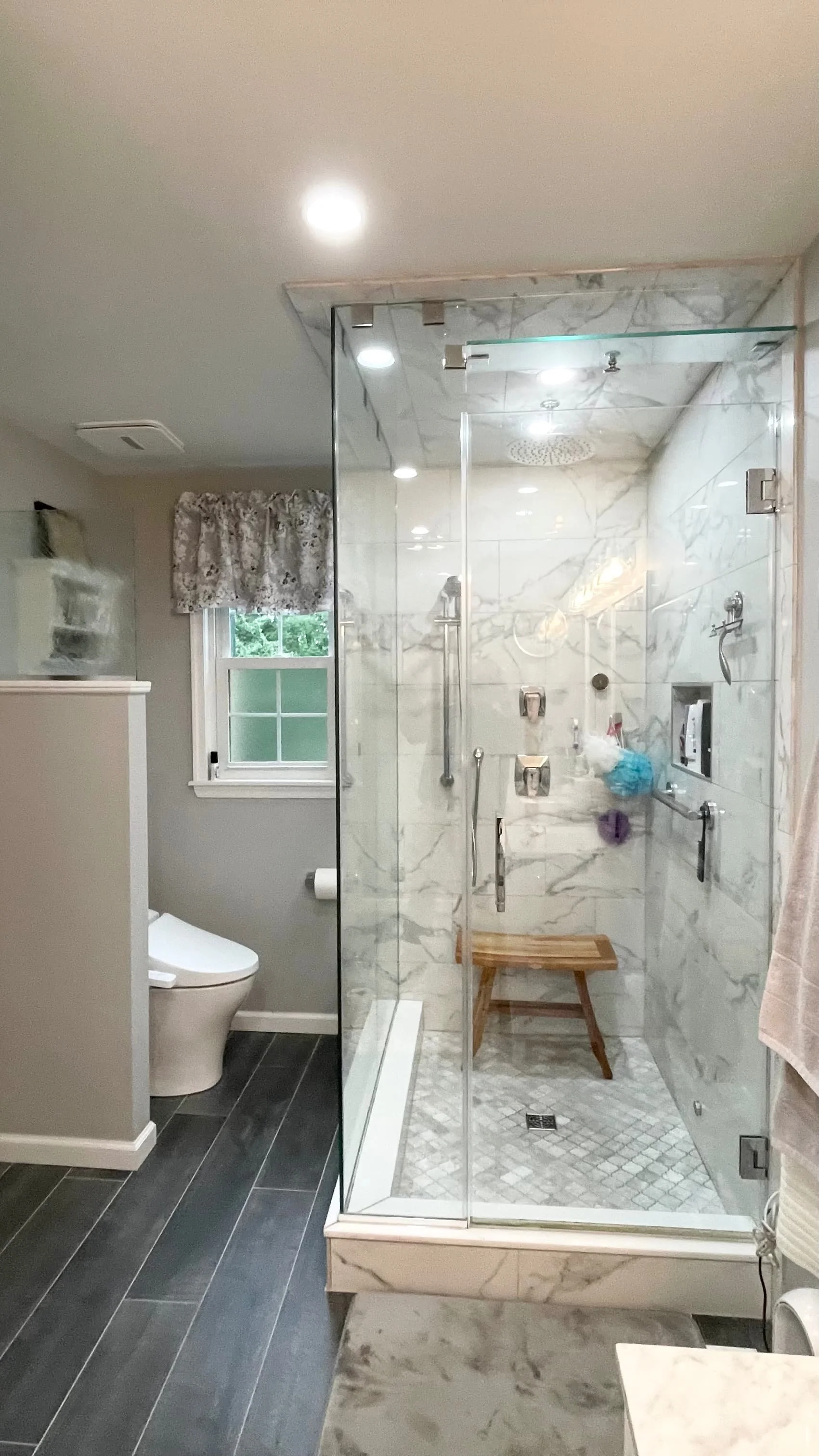 Finished frameless glass shower with marble-look tile and rainfall showerhead next to toilet in remodeled Hatboro, PA bathroom