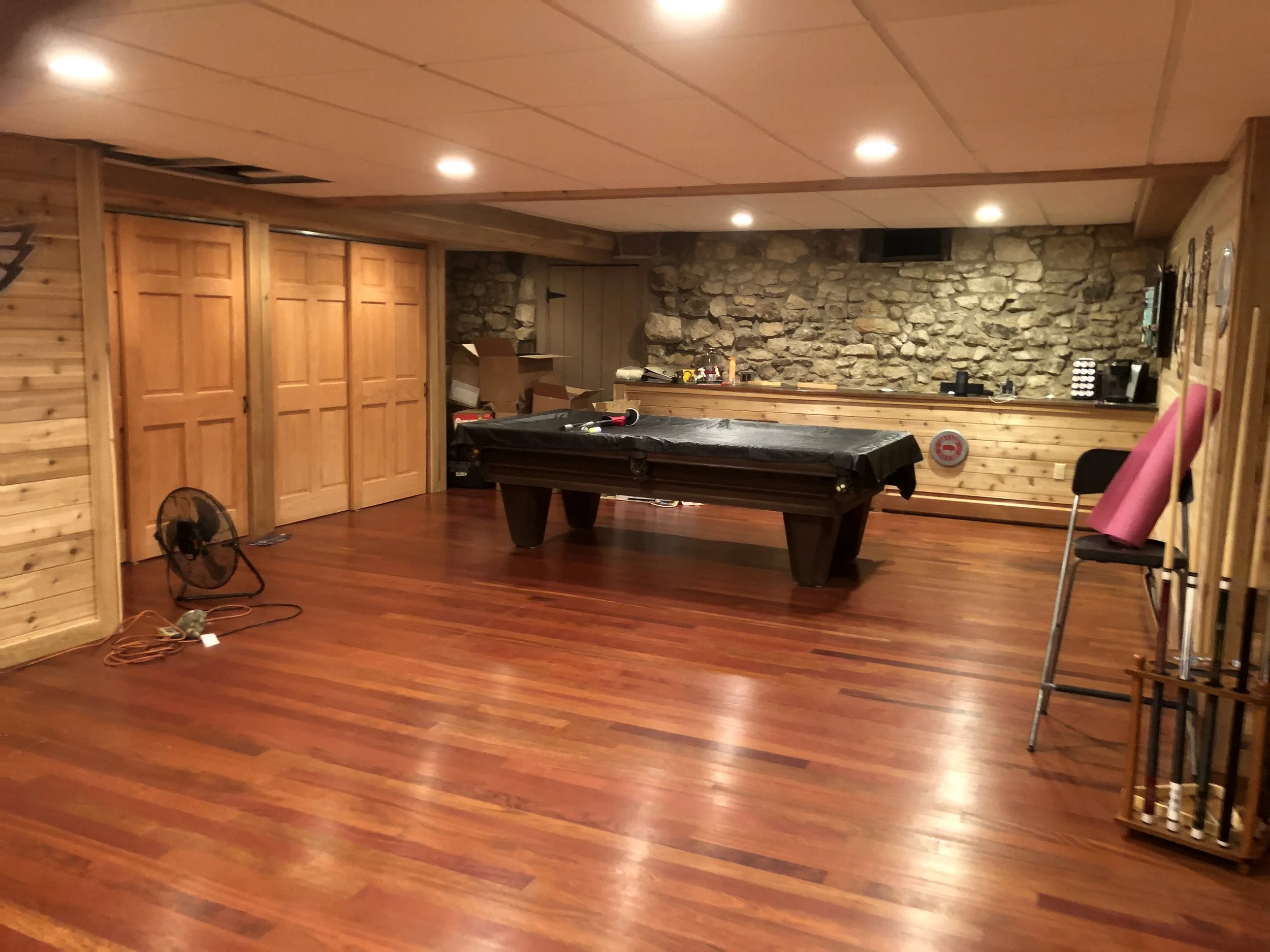 Finished basement rec room in Blue Bell, PA with pool table, stone accent wall, wet bar, and hardwood flooring.