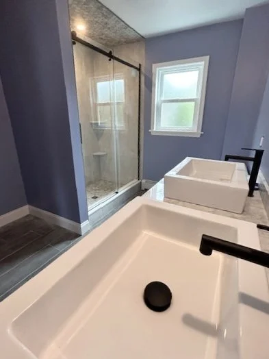 New bathrooom remodel in Hatboro, PA with white vessel sink, matte black faucet, marble countertop, and walk-in glass shower in background
