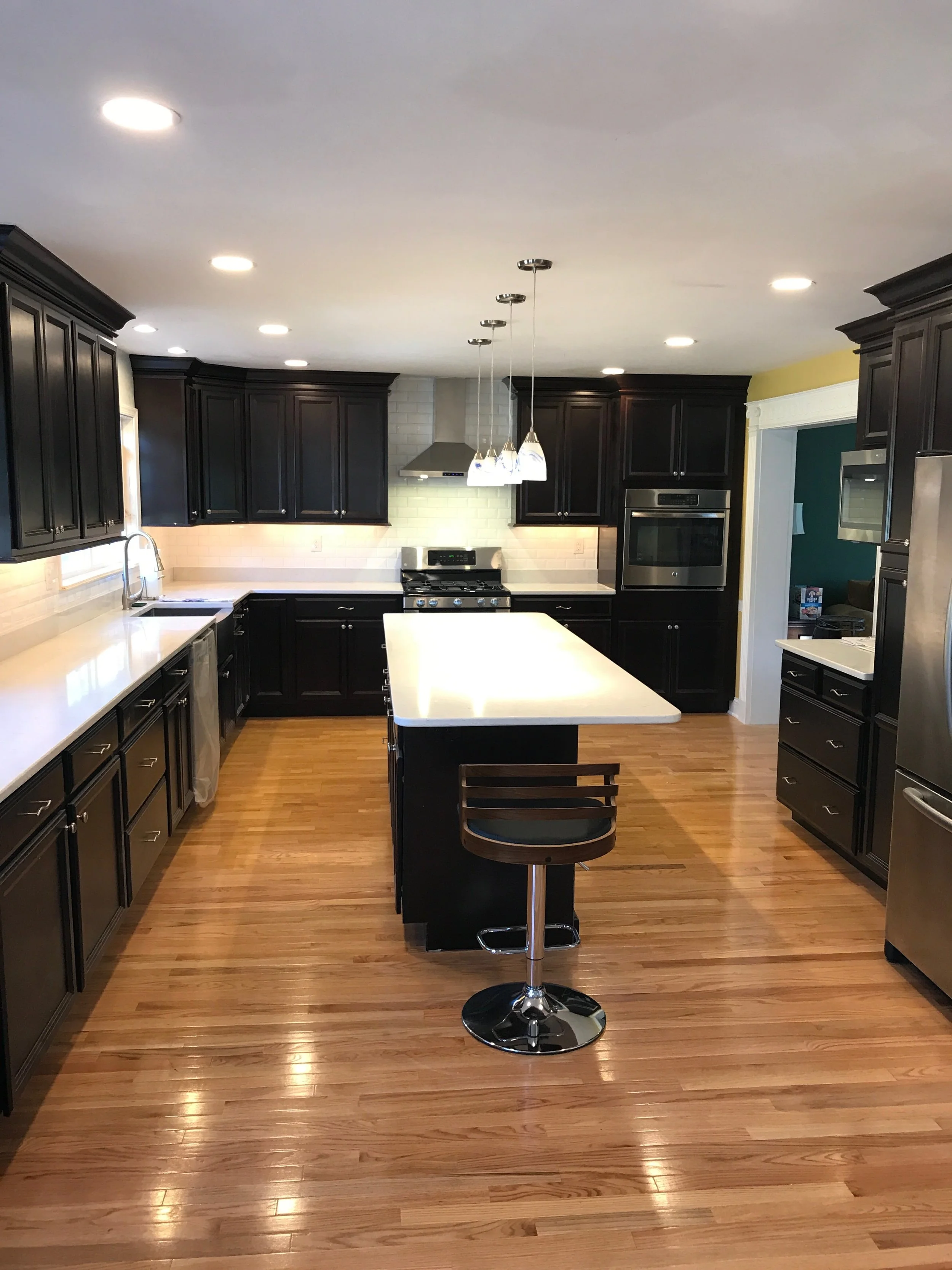 Completed JWD Contractors kitchen remodel with dark cabinetry, large center island, hardwood flooring, recessed lighting, and pendant lights.