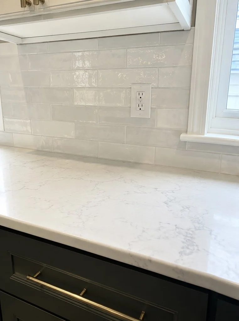 White and light gray subway tile backsplash meeting a light quartz countertop in a kitchen detail view.