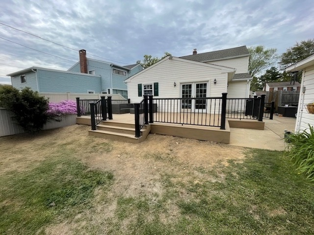 Backyard with a newly constructed wooden deck with black railings, beige steps, and a concrete walkway, adjacent to a white house with French doors and a window.