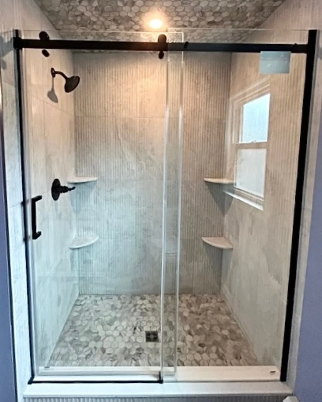bathroom remodel featuring custom tiled walk-in shower with pebble tile floor and ceiling, frameless glass sliding door, matte black fixtures