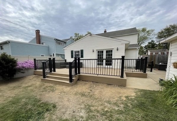 Composite deck in Willow Grove, PA with black aluminum railing, steps, and patio connection off read of home