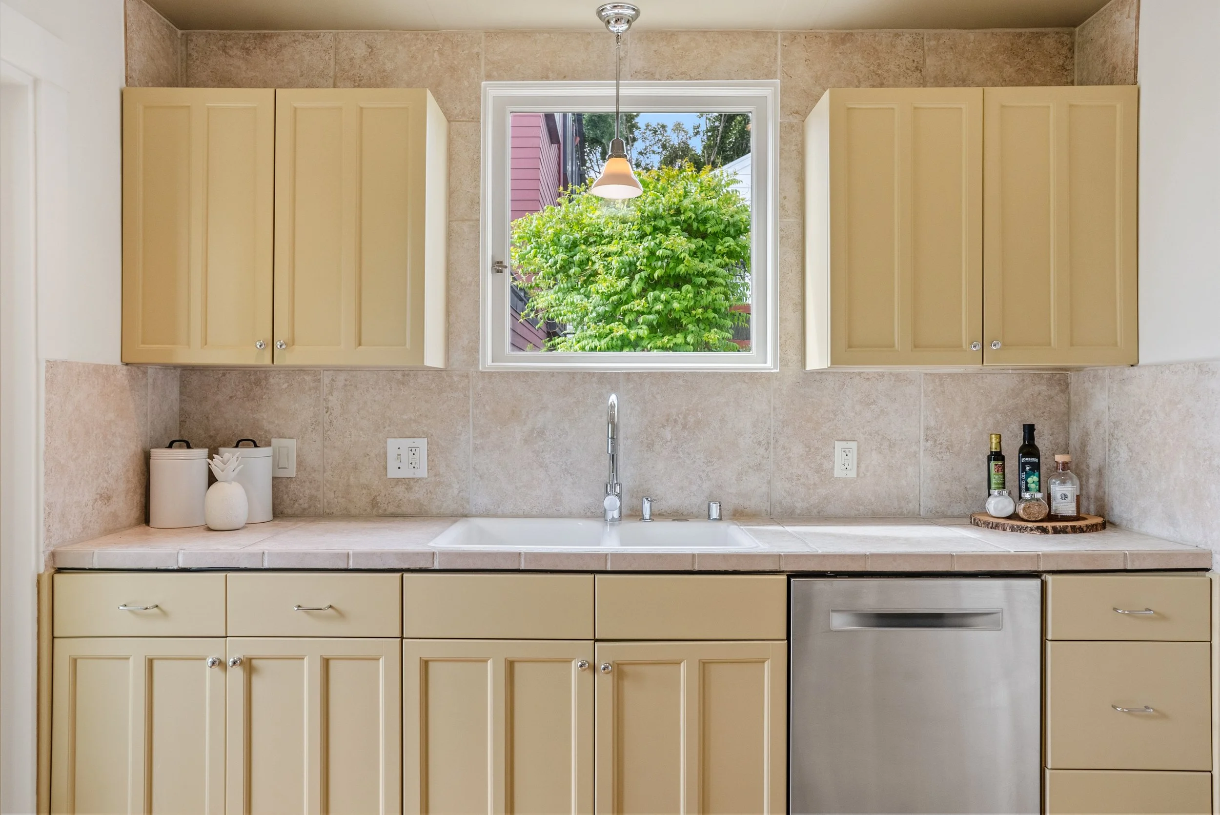 Modern kitchen with dark wood cabinets, a granite island with a sink, two white barstools, and stainless steel appliances including a microwave, overhead lighting, and pendant lights.