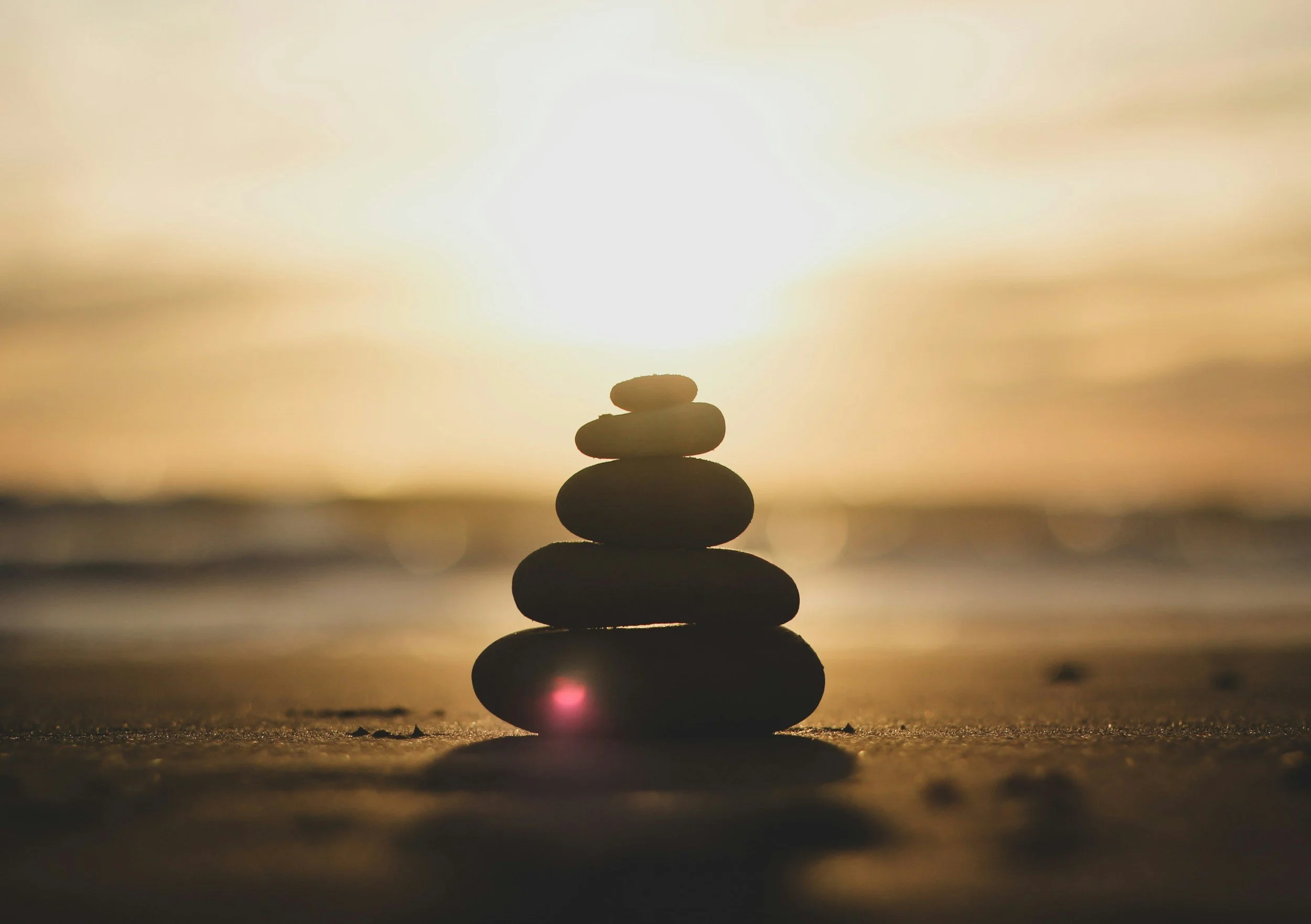 Stack of smooth stones balanced in a vertical line on a sandy surface with a setting sun in the background.