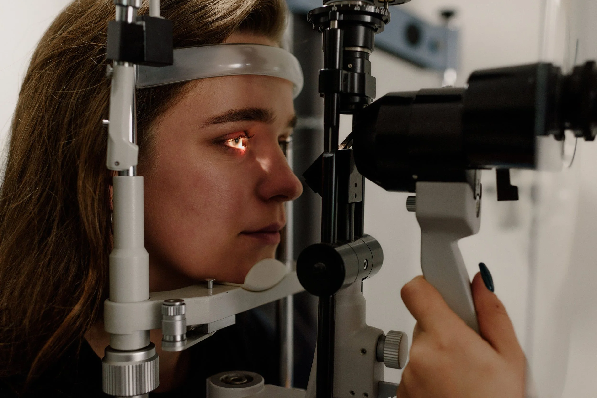 A woman with long brown hair looking through a medical eye examination device in a clinical setting.